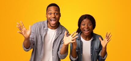 Surprised Black Couple Exclaiming With Excitement And Spreading Hands Over Yellow Studio Background And Looking At Camera, Overjoyed Emotional African Man And Woman Celebrating Success, Free Space photo