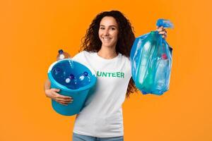 Female Volunteer Holding Used Plastic Litter And Bottles In Garbage Bag Smiling To Camera Standing Over Yellow Studio Background. Waste Sorting And Recycling, Volunteering Work Concept photo