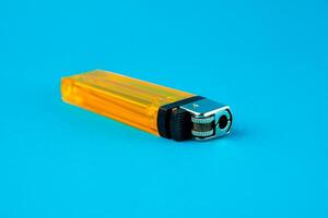 A transparent yellow plastic lighter standing upright against a bright blue background. The close-up shot highlights its metallic ignition mechanism and fluid inside, ideal for fire needs. photo