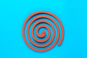 A single brown mosquito coil in a spiral shape on a blue background. Traditional insect repellent used for mosquito control, providing protection for indoor and outdoor environments. photo