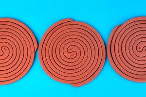 Three brown mosquito coils in a spiral shape on a blue background. Insect repellent for indoor and outdoor use, designed to keep mosquitoes away and provide protection from bites. photo