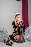 Woman in traditional Javanese attire poses gracefully with closed eyes and a peaceful smile. Her calm, meditative expression reflects elegance, cultural richness, and inner serenity. photo