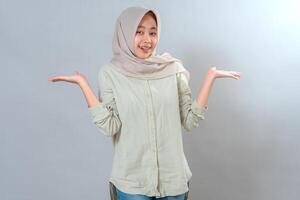 Young Muslim woman in hijab smiling with a confused expression, raising both hands in a shrugging gesture. Her friendly face conveys uncertainty, curiosity, and open-mindedness. photo