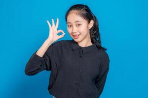 Smiling young Asian woman making an OK hand gesture while looking at the camera. Her friendly and confident facial expression conveys positivity, approval, and satisfaction. photo