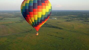 A colorful air balloon is flying in free flight over the field. Bird's-eye view. Multi colored balloon in the blue sky. video