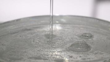Thin trickle of transparent cosmetic gel with tiny bubbles flows down to the surface. Transparent liquid gel background, transparent serum texture. Cosmetic skin care product. top view video