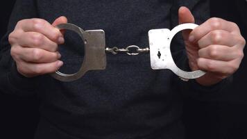 The hands of an unknown man are holding steel handcuffs. The handcuffs are bound with a strong chain, symbolizing power and control. The concept of crime and punishment video