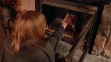 Over shoulder shot. blond woman carefully arranging firewood inside rustic fireplace, methodically preparing to ignite flames, creating warm and inviting ambiance during cold evening in slow motion video