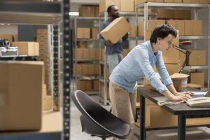 Female staff member coordinating and verifying custom orders in local brand warehouse, handling cardboard boxes for small business logistics and delivery services in distribution hub. photo