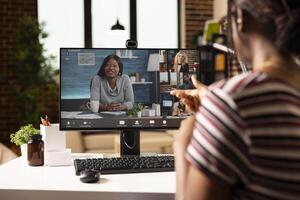 Back view of businesswoman in home workspace, discussing project plans with teammates in conference. Multiethnic team members join online meeting, working remotely from individual locations. photo