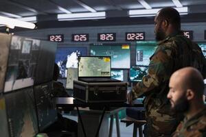Air force combat control officer performing tactical level surveillance in war room using laptop. Military specialist in base of operations using radar on notebook to look at assault zones photo