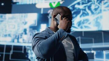 Black entrepreneur using mobile phone call to interact with people, shares insight on cybernetic platforms and AI interfaces. Machine learning and predictive analytics for growth. Camera A. video