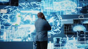 African American businessman studying digital AI brain interface, symbolizing neural networks, data science and algorithmic thinking. Cybernetics for a high tech futuristic innovation. Camera A. video