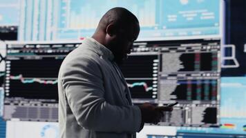 Young business leader checking online fintech reports on mobile phone, examining infographics for financial insight and development. Young adult browses smartphone apps. Camera B. video