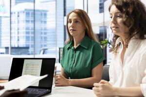 HR staff members reading resume, determining if candidate possesses skills and experience needed to fulfil role. Employer talking with man, checking CV, evaluating if qualifications align with company photo
