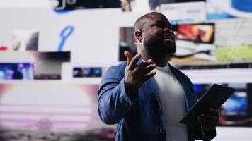 African american public speaker discussing with audience about social media platforms, dynamic screens for entertainment and web communication. Networking advice for engagement. Camera B. video