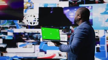 African American tech enthusiast looking at chroma key screen next to digital interfaces and multimedia visuals, showcasing content creation, mobile technology and global online influence. Camera A. video