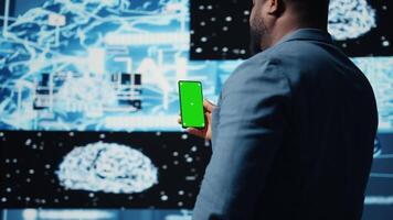Focused black IT professional looks at phone with green screen, standing in a digital artificial intelligence environment. Solving deep learning tasks for big data automation. Cybernetics. Camera A. video