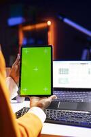 Self employed person at home checks statistics on laptop while using chroma key tablet. Remote worker holding isolated screen device, analyzing business graphics, close up shot photo