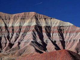 A Desert Mountain's Ancient Layers Unveiled Under a Vast Blue Sky with Contrail photo