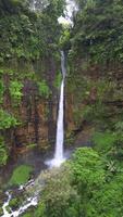 Cinematic aerial view of Kapas Biru waterfall cascading down a tall cliff into a lush green canyon, surrounded by tropical rainforest in East Java, Indonesia. video