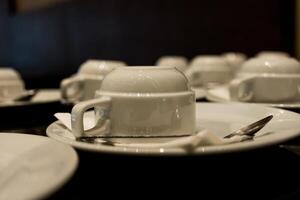 White coffee cups and saucers are placed upside down on table. photo