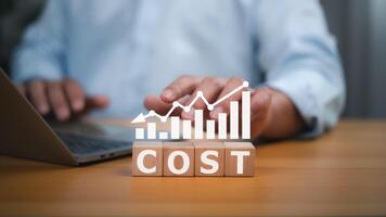 People working and wooden blocks spelling out the word COST, with a graph overlaying a downward trend, representing declining costs, cost analysis, financial management challenges, and economic trends photo