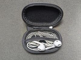 Open Earphone Case with White Wired Headphones on a Gray Textured Surface photo