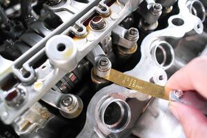 Closeup of engine valve adjustment with feeler gauge, mechanic working and car repair, automotive maintenance in auto service garage. photo