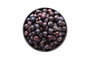 dried juniper berries in clay bowl isolated on white background. Seasoning or spice top view photo