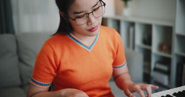 Handheld selective focus shot, Young Asian woman is relaxing and enjoying playing music on an electronic keyboard in a quiet house. Leisure activities at home video