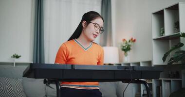 Handheld low angle view shot, Young Asian woman is relaxing and enjoying playing music on an electronic keyboard in a quiet house. Leisure activities at home video
