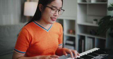 Handheld selective focus shot, Happy woman in an orange shirt is practicing her keyboard skills intently in a living room. Enjoy favorite musical instruments video