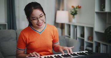 Happy young woman in an orange shirt is practicing her keyboard skills intently in a living room. Enjoy favorite musical instruments video