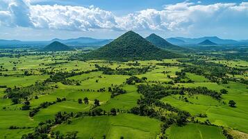 Lush green landscape with cone shaped hills and dramatic clouds. This aerial view showcases the vibrant expanse of cultivated fields and scattered trees under a partly cloudy sky. photo