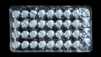 A sterile blister pack contains multiple white round pills with a dividing line. The medical supply is presented on a stark black background, highlighting its clinical appearance. photo