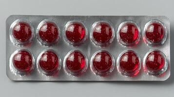 Shiny Red Capsules in Blister Pack. This image shows a pharmaceutical blister pack containing multiple bright red, gelatinous capsules with a subtle glitter effect. photo