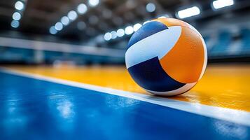 Close up of a volleyball resting on a brightly lit indoor court floor. The focus is on the textured surface of the ball and the vibrant colors of the court. photo
