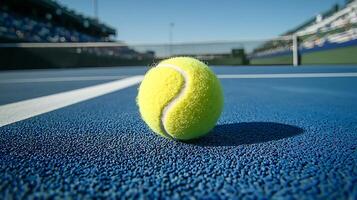 Close up of a tennis ball on a blue court. The background shows a blurred tennis stadium and net. photo