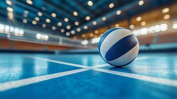 A detailed close up of a volleyball on a bright blue court. The background shows a blurred sports arena with warm lights. photo