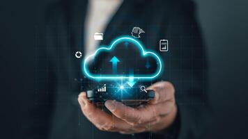 A businessman holds a smartphone with a glowing cloud icon, symbolizing cloud computing, data storage, digital solutions, and online technology for modern business and virtual connectivity photo