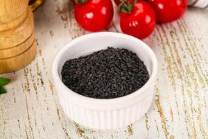 Black cumin seeds in a white bowl on a wooden table photo
