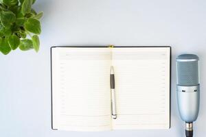 Studio microphone and open notebook on a light background indoors, flat lay. Copy space. Podcast concept photo