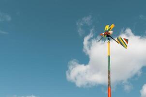 Homemade, multi-colored wooden weather vane on a pole against a blue cloudy sky. Copy space for text. photo
