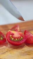 Close-up of a hand slicing ripe tomatoes on a wooden board with a sharp knife under bright lighting video