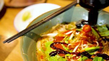 A close-up of sauce being drizzled over a vibrant bowl of Vietnamese pho, highlighting fresh ingredients and rich colors under warm lighting video