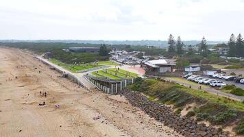 Aerial footage captures Ocean Grove beach, parking area, and nearby structures under bright daylight, showcasing a serene coastal environment video