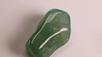 A green aventurine stone spins smoothly on a white surface, highlighting its glossy texture and natural patterns video