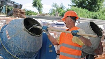 Construction Worker Mixing Cement in Drum Mixer, Wearing Orange Safety Vest and Helmet at Building Site video