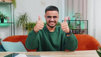 Like. Happy excited Indian man looking approvingly at camera showing thumbs up like sign positive something good great news positive feedback. Young Arabian guy sitting at home office room at table video